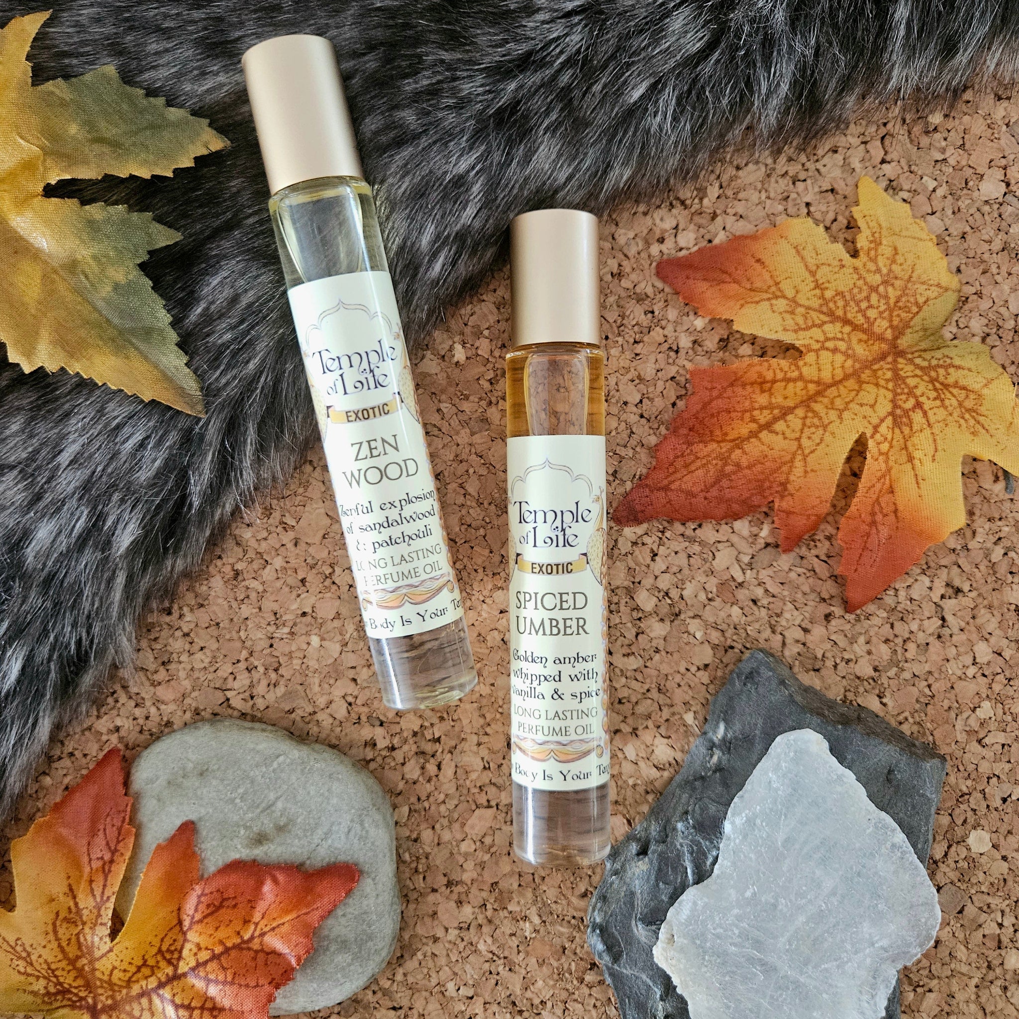 Two bottles of Fall perfumes by Temple & Life on a textured surface with autumn leaves and stones.
