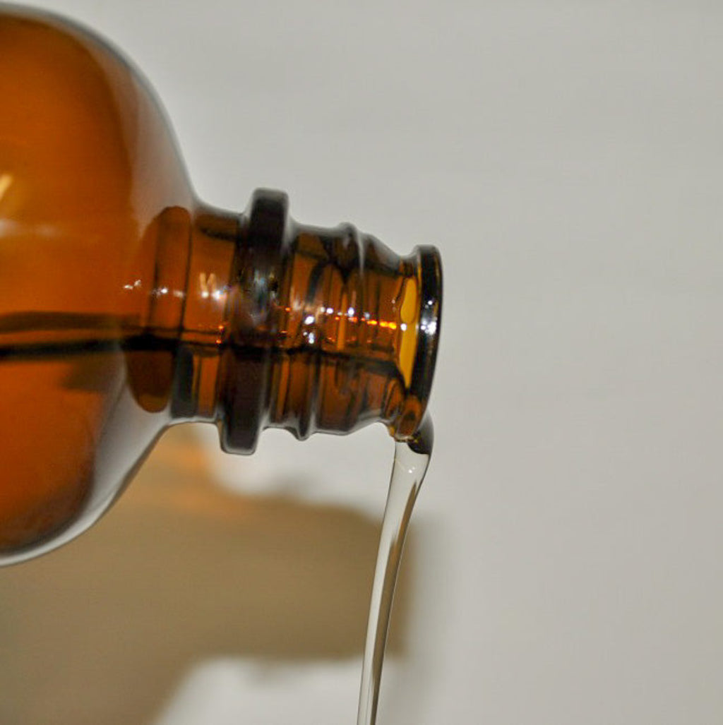Close-up of a brown glass bottle pouring body oil on a light gray background
