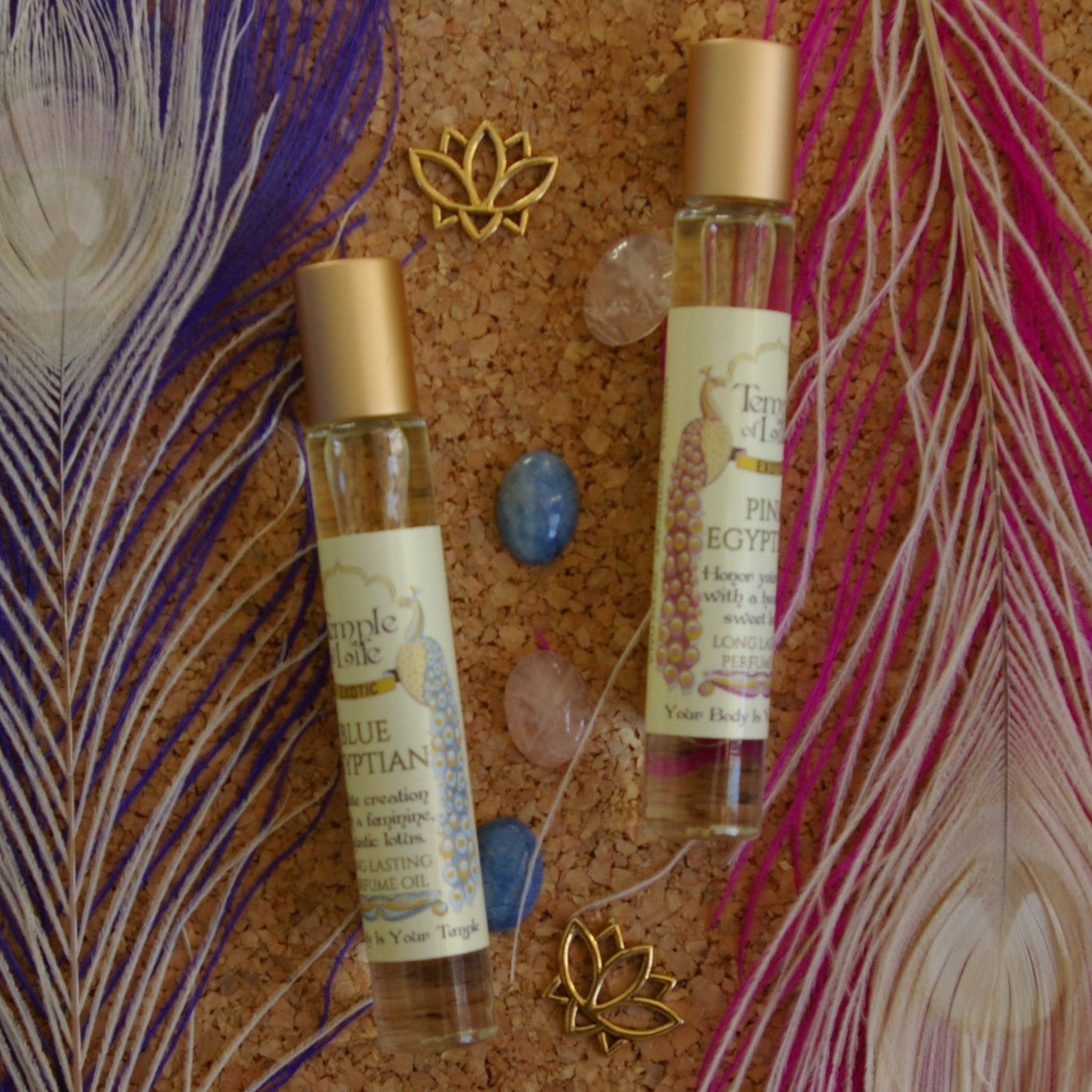 Two small bottles of lotus perfume with decorative feathers and stones on a cork background