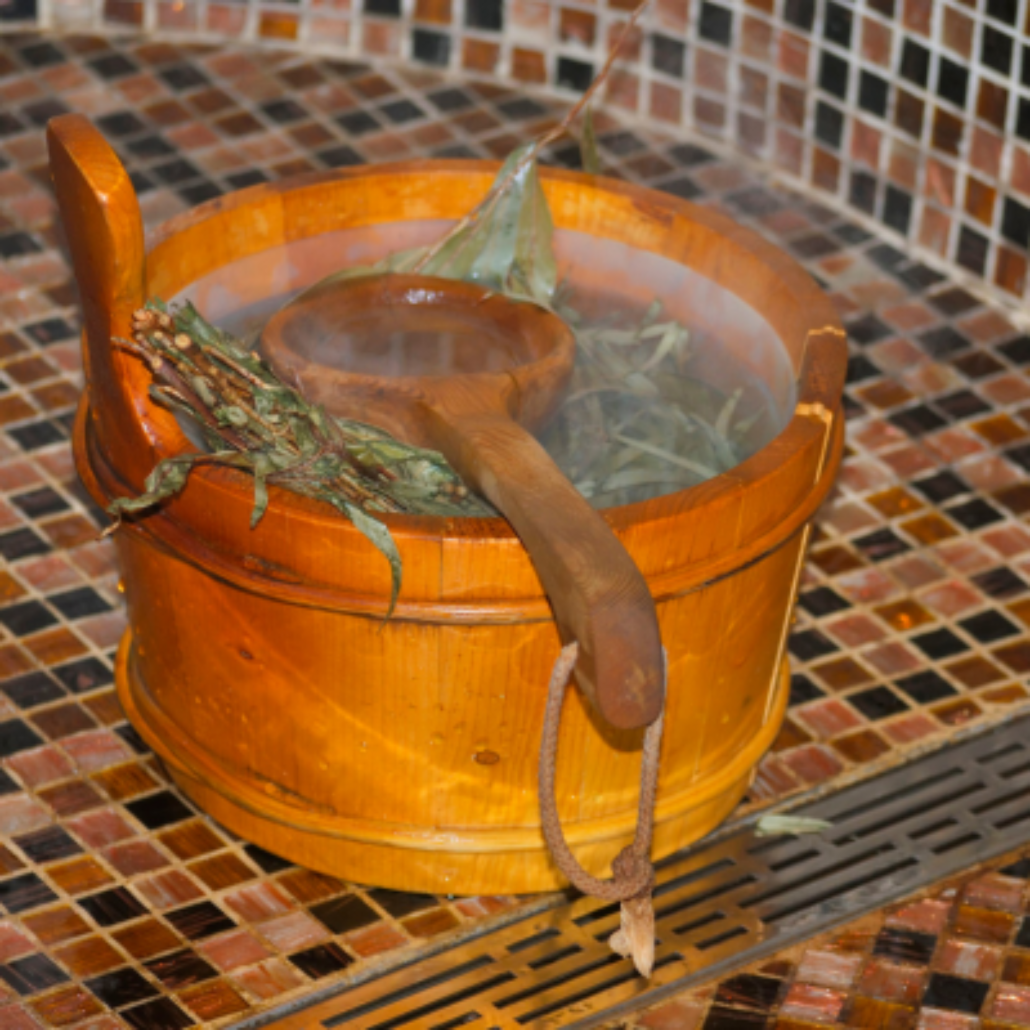 Wooden bucket filled with spa herbs with a ladle on a tiled floor