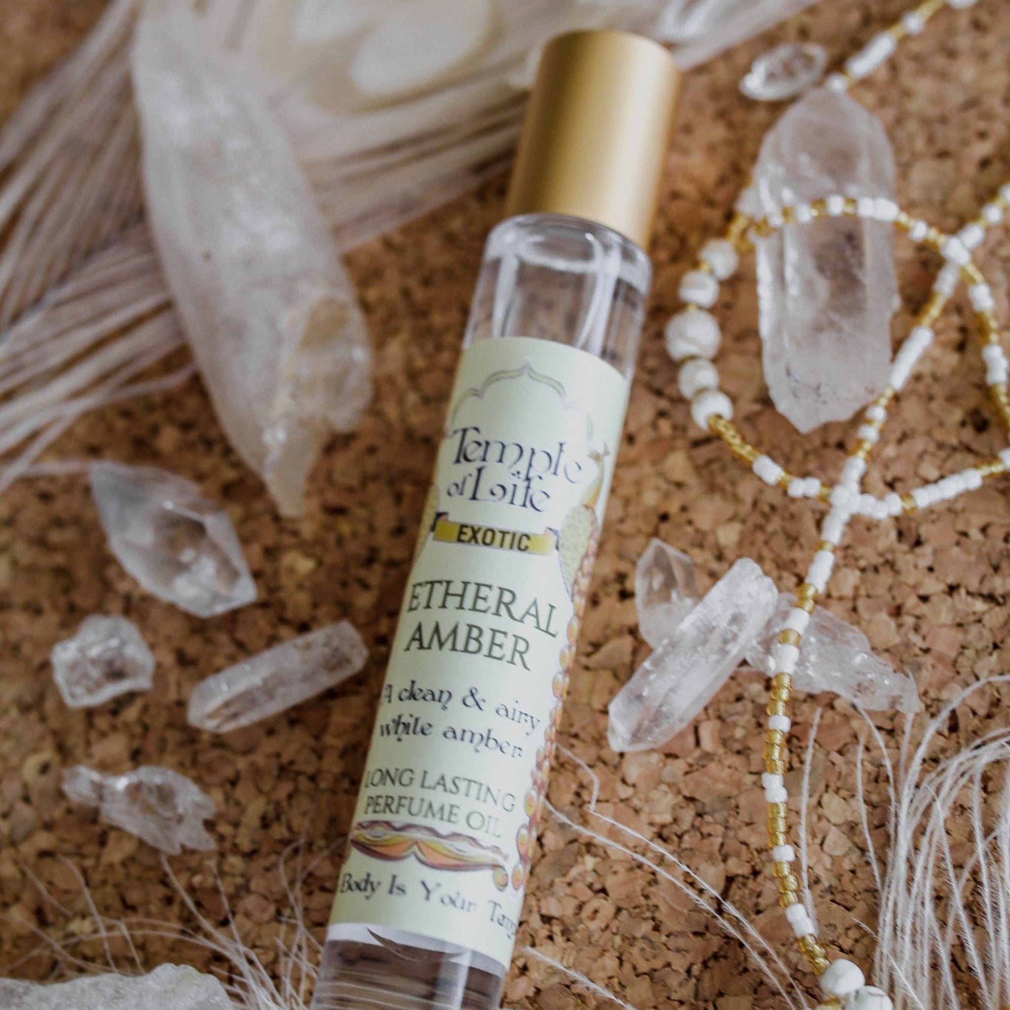 Perfume bottle labeled 'Etheral Amber' on a cork board with crystals and tassels.