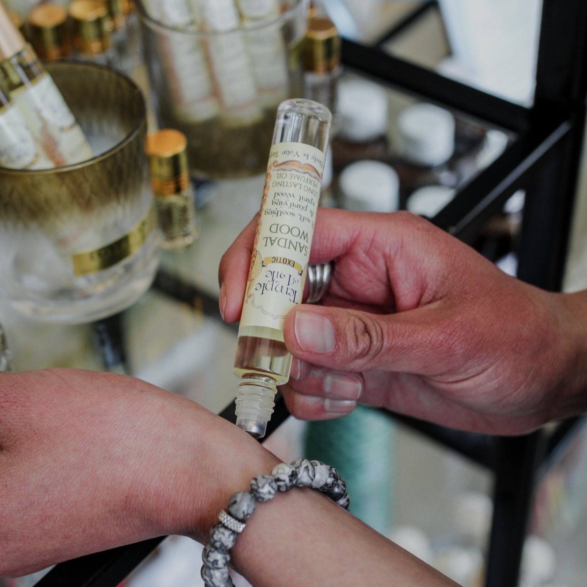 Person applying a roll-on bottle of Sandalwood perfume by Temple of Life Oils on their wrist.