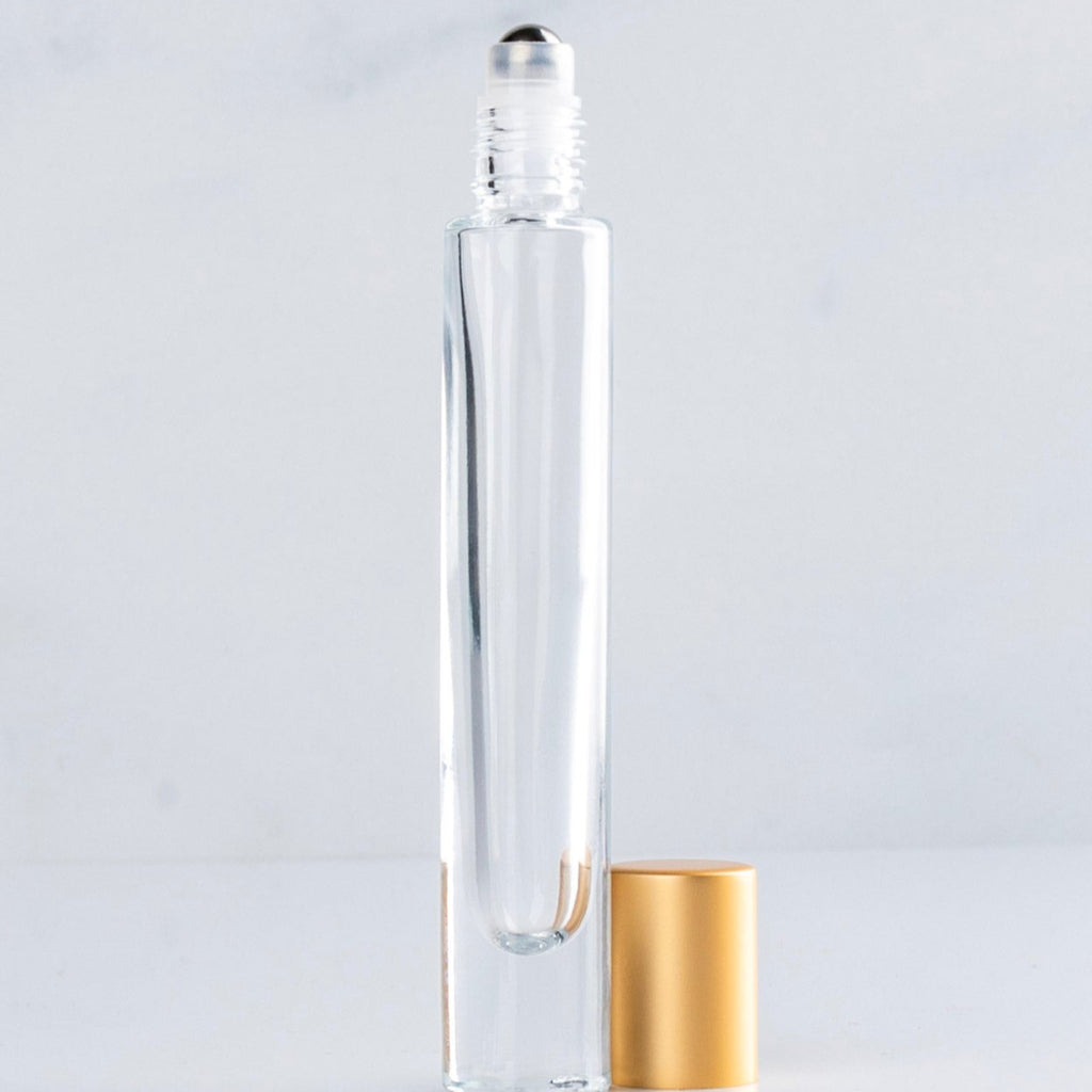 Clear glass roller bottle with gold cap on a light gray background